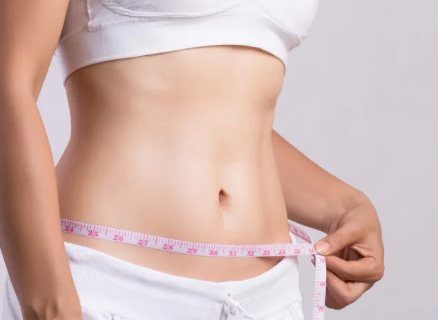 A woman in white athletic wear measuring her waist with a pink measuring tape, showing a slim and toned stomach.